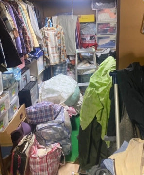 遺品整理前：ハンガーに掛かった大量の洋服や、枕棚の上にまで詰め込まれた収納袋、床に置かれた生活用品で溢れている状態の和室